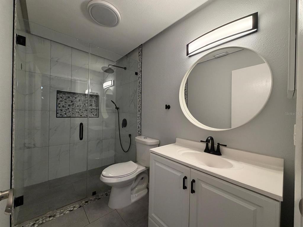 A modern bathroom features a glass-enclosed walk-in shower, a white vanity, and a round mirror — 8643 MALLARD RESERVE DRIVE UNIT 202, TAMPA, FL