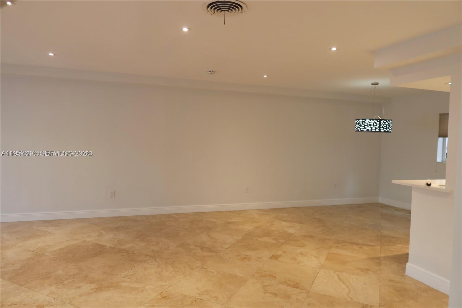 An empty room features beige tile flooring, recessed lighting, and a decorative pendant light fixture — 7312 Gary Ave # 7312, Miami Beach FL 33141, MIAMI BEACH, FL