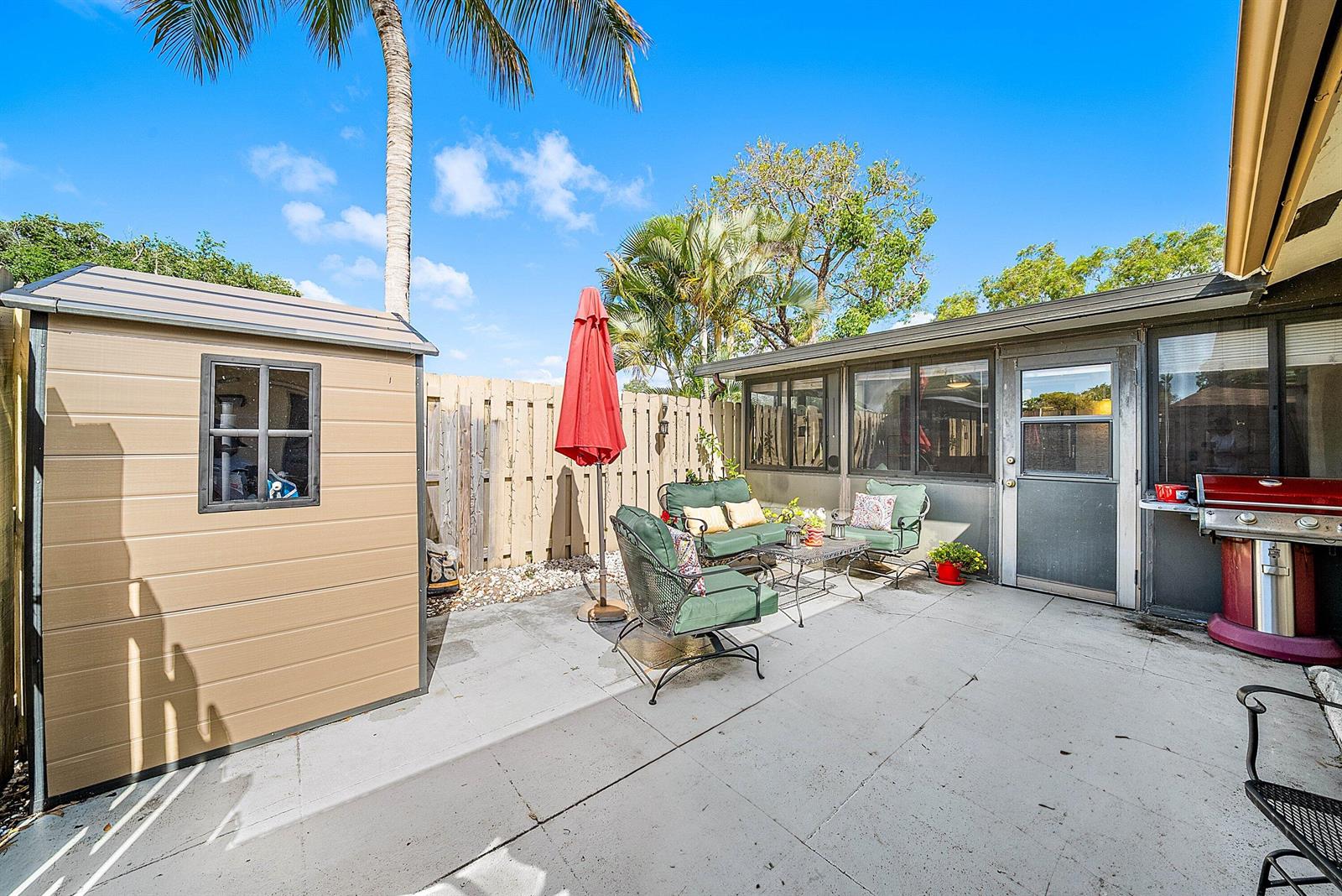 A patio features a storage shed, outdoor seating, a red umbrella, and a gas grill — 777 NW 29th Avenue # A, Delray Beach FL 33445, DELRAY BEACH, FL