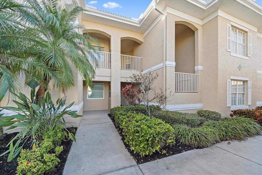 A two-story tan stucco building with a palm tree and a concrete walkway — 6318 GRAND OAK CIRCLE UNIT 204, BRADENTON, FL