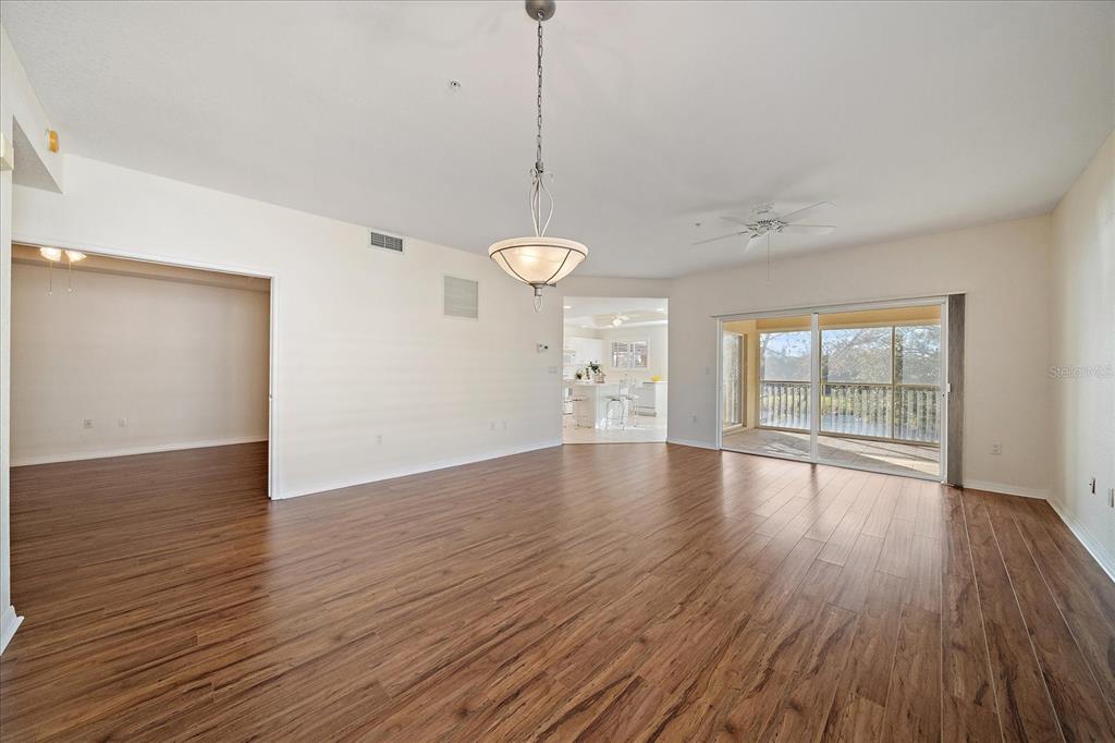 An open-concept living area features wood-look flooring, a chandelier, and sliding glass doors to a balcony — 6318 GRAND OAK CIRCLE UNIT 204, BRADENTON, FL