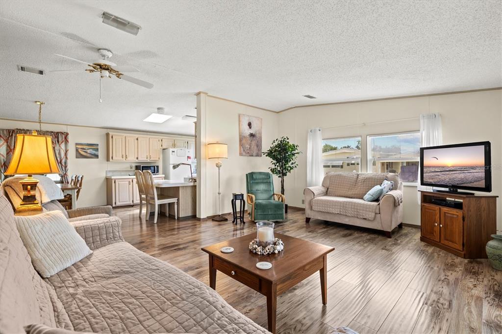 A living room with wood-look flooring, a coffee table, and an open view of the kitchen — 58 PARTRIDGE AVENUE, ELLENTON, FL