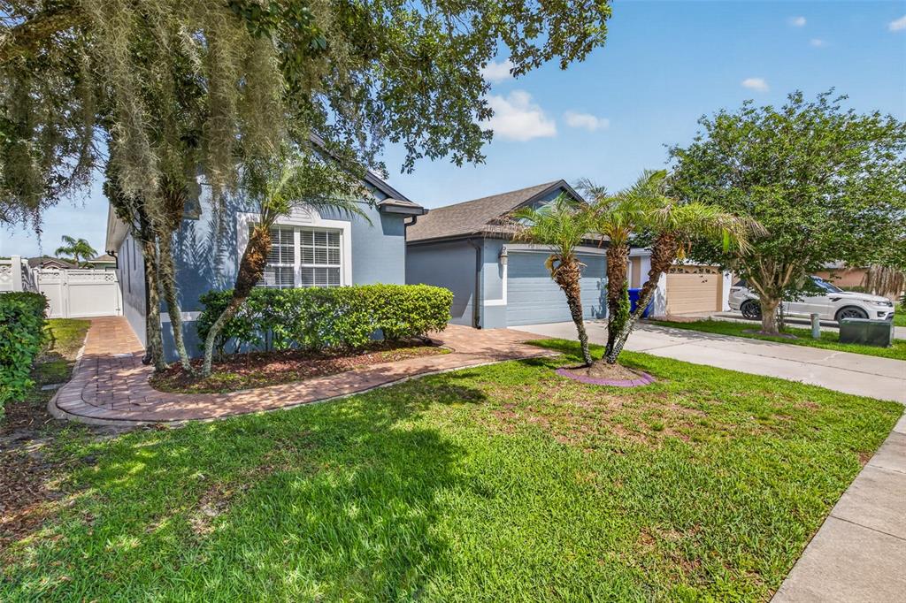 A blue single-story house with a paved walkway, palm trees, and a two-car garage — 2922 WILLOW CREEK LANE, KISSIMMEE, FL