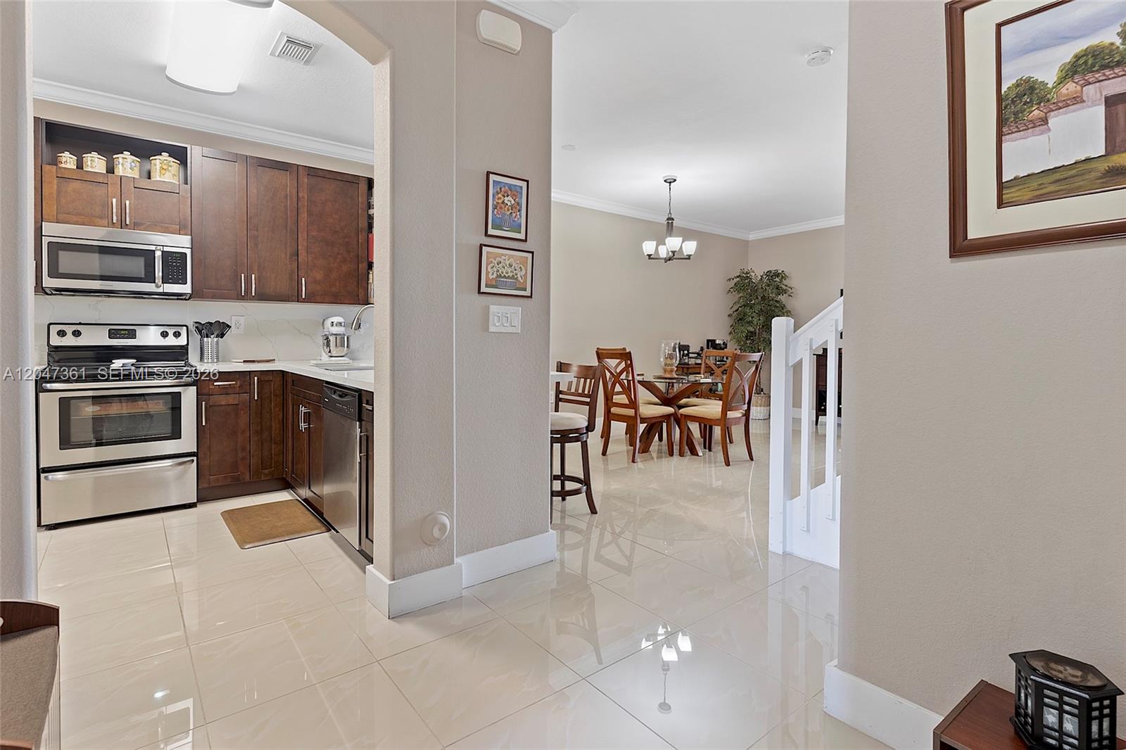 A kitchen with dark wood cabinets and stainless steel appliances opens to a dining area — 15262 SW 91st Ln, Miami FL 33196, MIAMI, FL