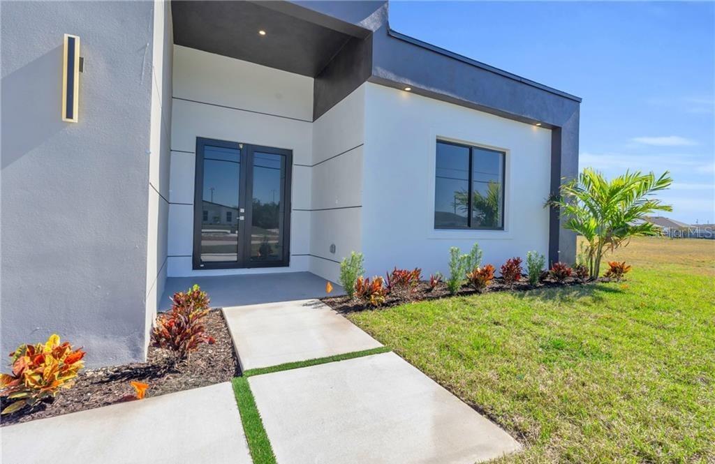 A modern house exterior features a concrete walkway leading to a dark-framed double front door — 3924 NW 38TH STREET, CAPE CORAL, FL