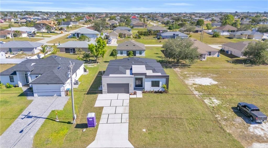 An aerial view shows a modern single-story house with a concrete driveway and surrounding neighborhood — 3924 NW 38TH STREET, CAPE CORAL, FL