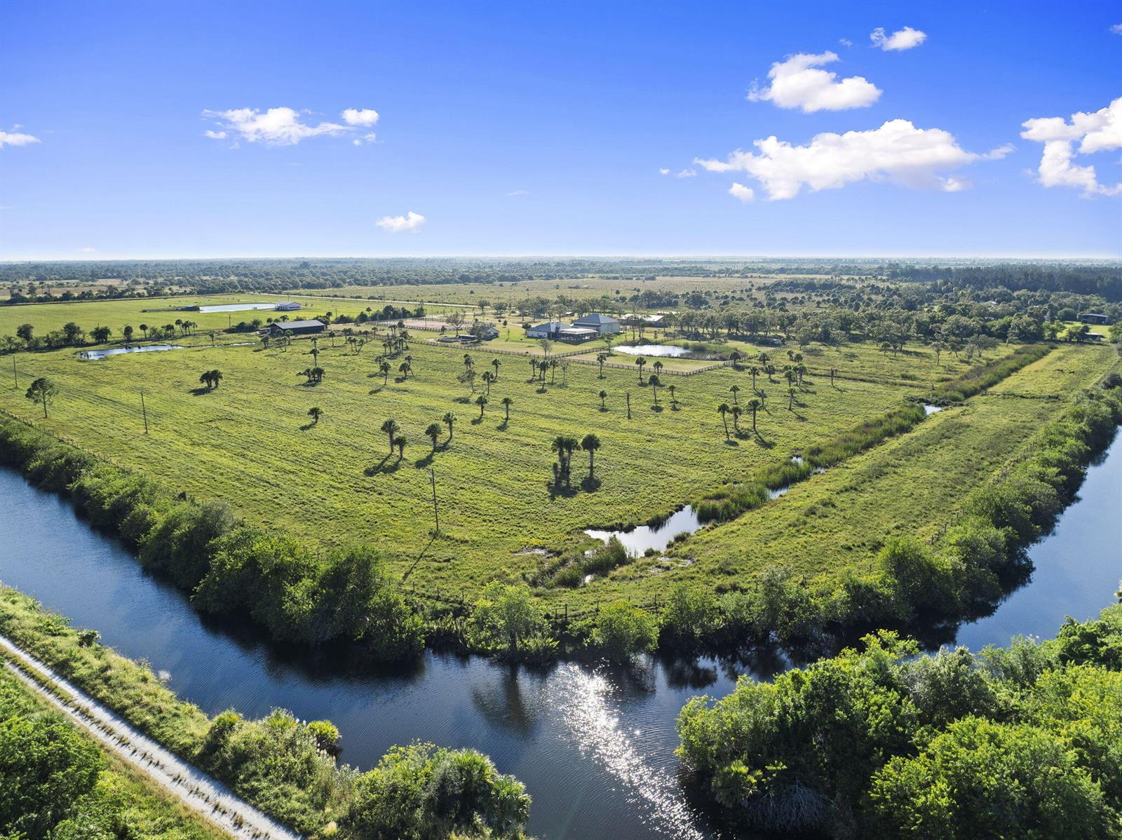 An aerial view shows a large, grassy pasture with scattered palm trees and a canal — 4044 Johnston Road, Fort Pierce FL 34951, FORT PIERCE, FL