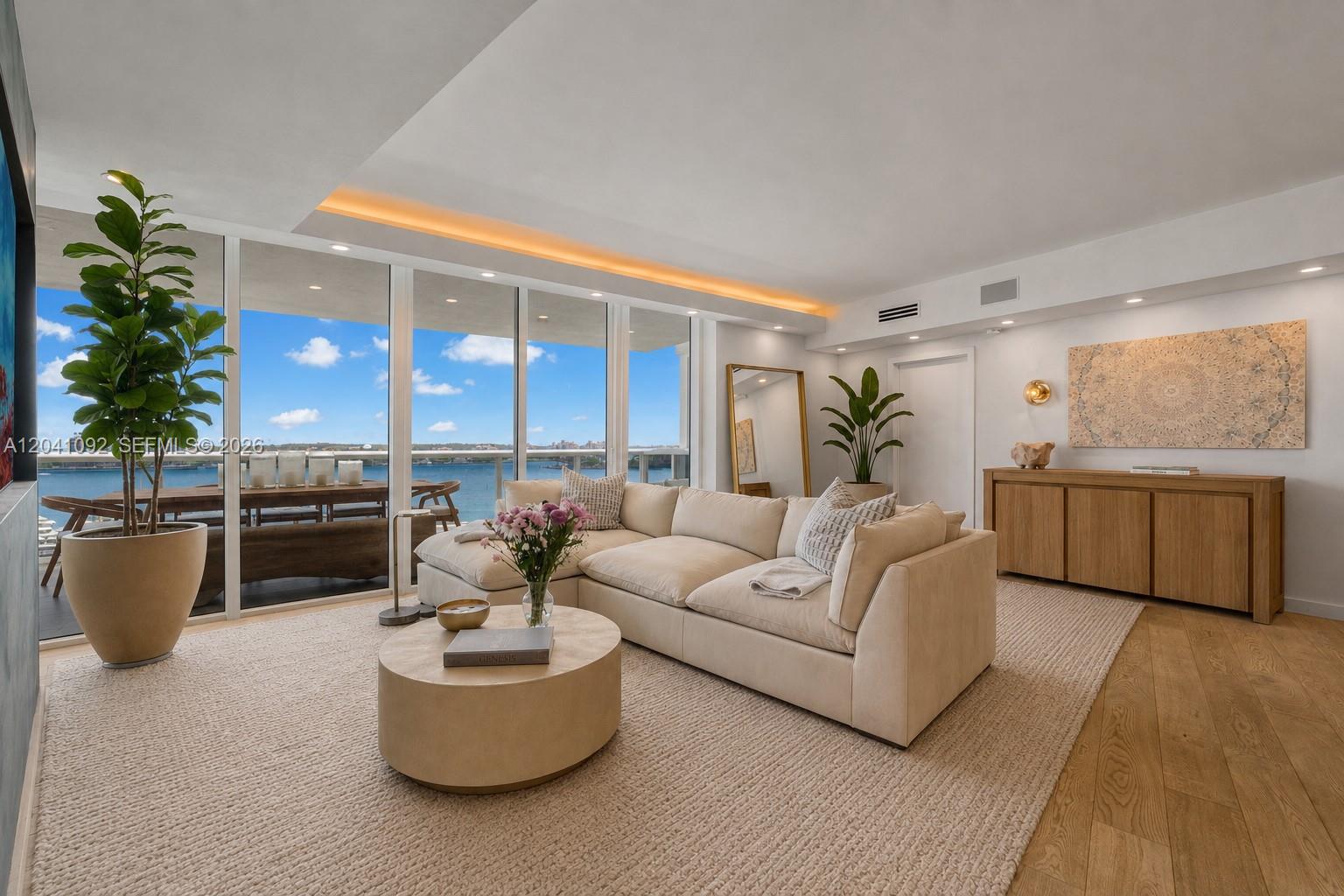 A living room features a beige sectional, round coffee table, and floor-to-ceiling windows overlooking water — 400 Alton Rd # 1206, Miami Beach FL 33139, MIAMI BEACH, FL