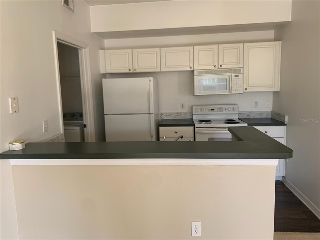 A kitchen with white cabinets, white appliances, and a dark countertop breakfast bar — 5578 METROWEST UNIT 206, ORLANDO, FL