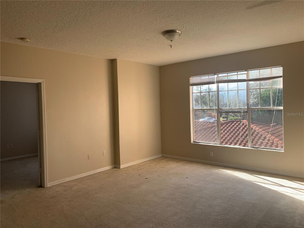 An empty bedroom features beige walls, tan carpeting, and a large window with blinds — 5578 METROWEST UNIT 206, ORLANDO, FL