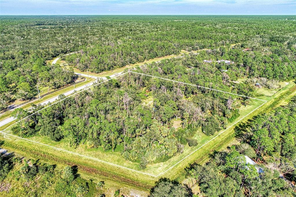 An aerial view shows a rectangular, wooded lot outlined in white near a paved road — Lot 2 TROPICAIRE BOULEVARD, NORTH PORT, FL