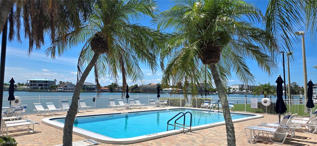 A swimming pool with lounge chairs sits on a patio overlooking a waterfront residential area — 400 64TH AVENUE UNIT 103w, ST PETE BEACH, FL