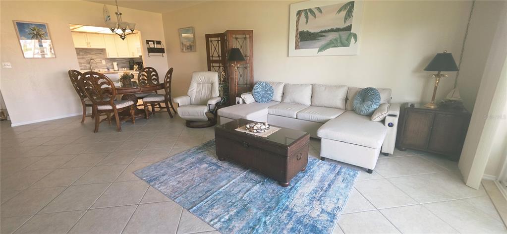 A living room with a sectional sofa, coffee table, and adjacent dining area with tile floors — 400 64TH AVENUE UNIT 103w, ST PETE BEACH, FL