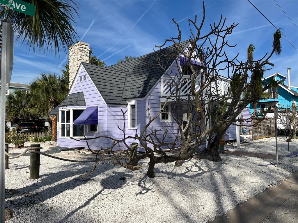 A light purple house with a dark roof and a stone chimney sits on gravel — 8401 W GULF BOULEVARD, TREASURE ISLAND, FL
