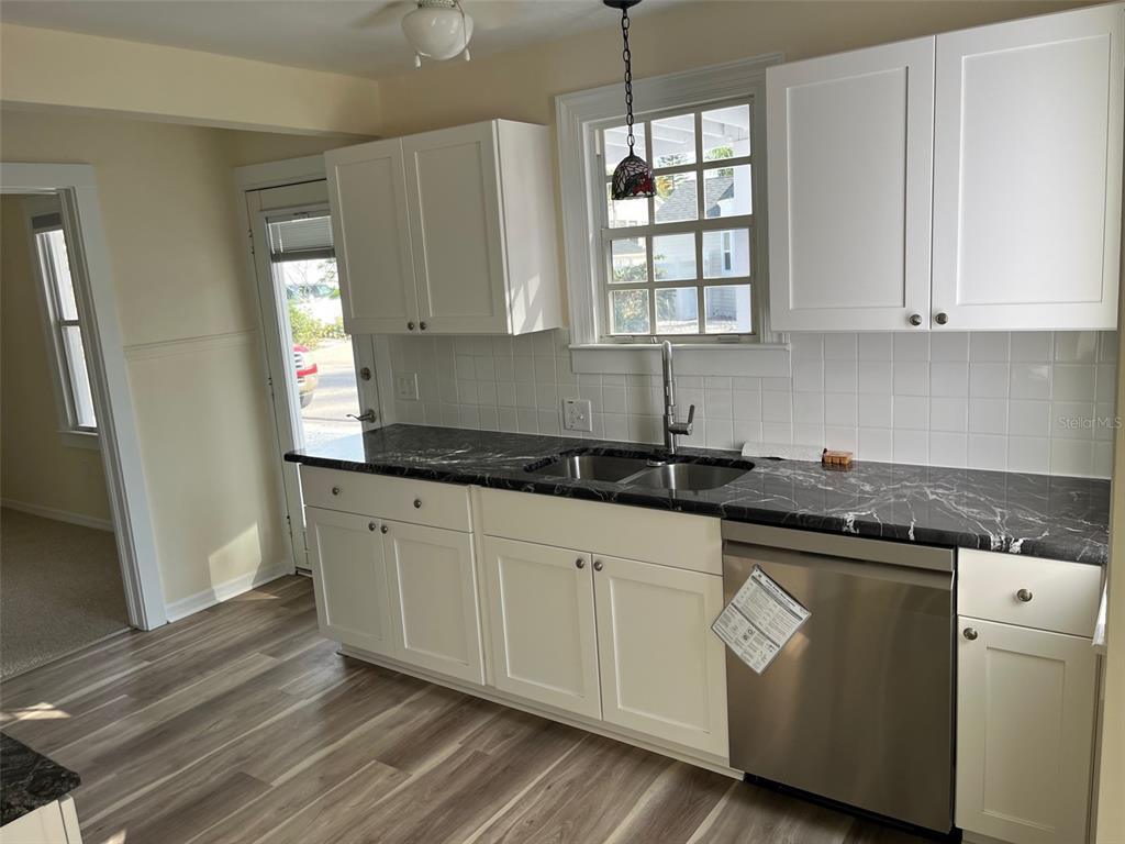 A kitchen features white cabinets, black marble-patterned countertops, a stainless steel dishwasher, and a window — 8401 W GULF BOULEVARD, TREASURE ISLAND, FL