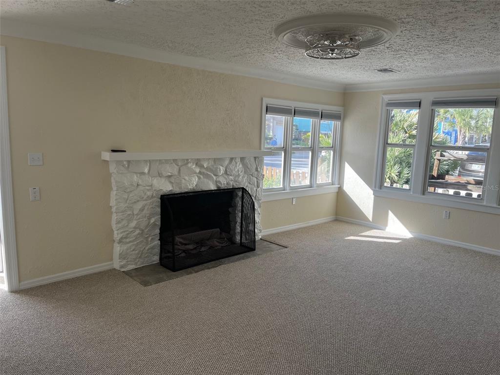 A living room features a white stone fireplace, beige carpet, and large windows — 8401 W GULF BOULEVARD, TREASURE ISLAND, FL