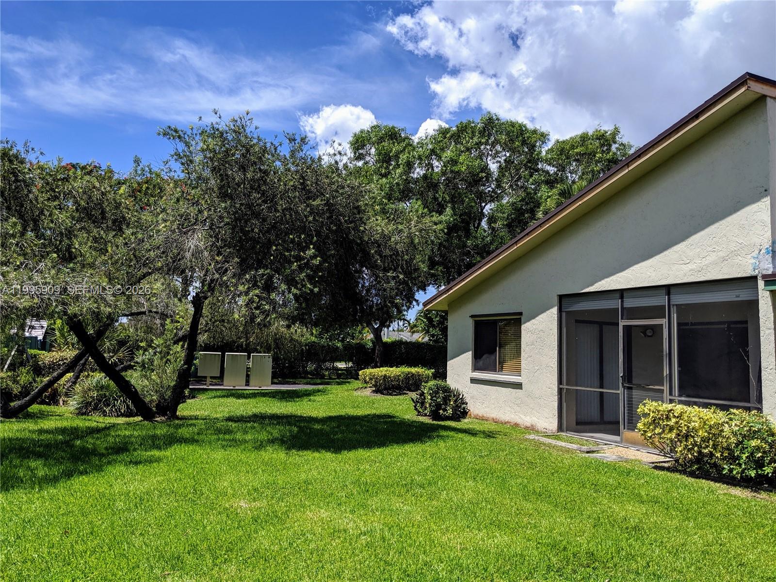 A grassy backyard features a house with a screened-in patio and mature trees — 460 Lakeview Dr # 4, Weston FL 33326, WESTON, FL