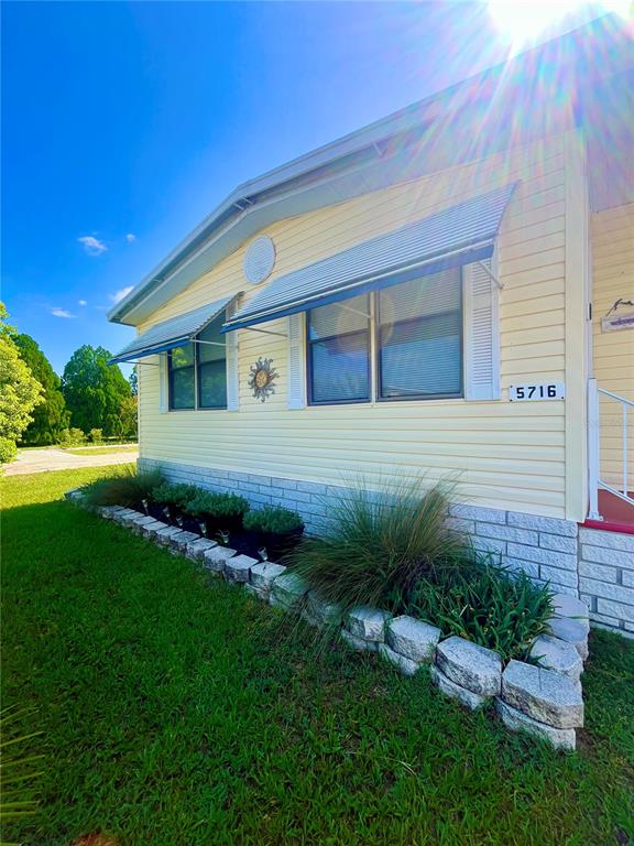 The exterior of a yellow mobile home features metal window awnings and a stone planter — 5716 PAWNEE STREET, ZEPHYRHILLS, FL