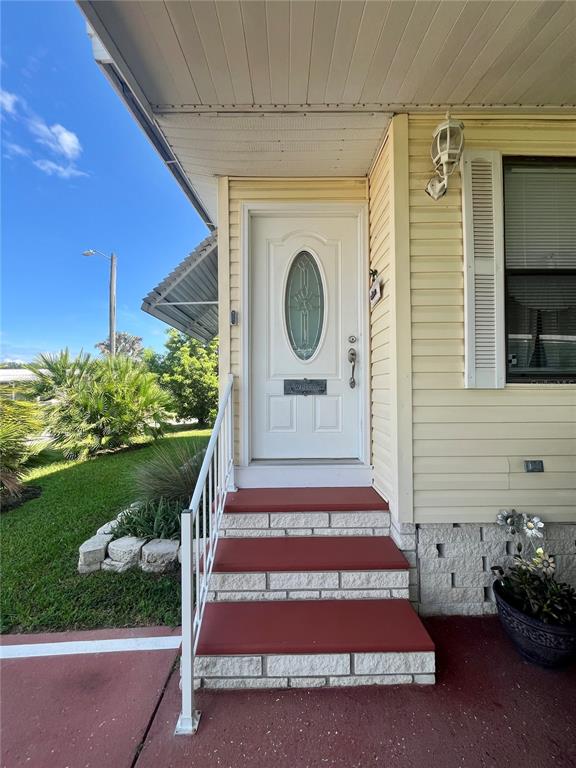 A white front door with an oval window sits atop three red steps — 5716 PAWNEE STREET, ZEPHYRHILLS, FL
