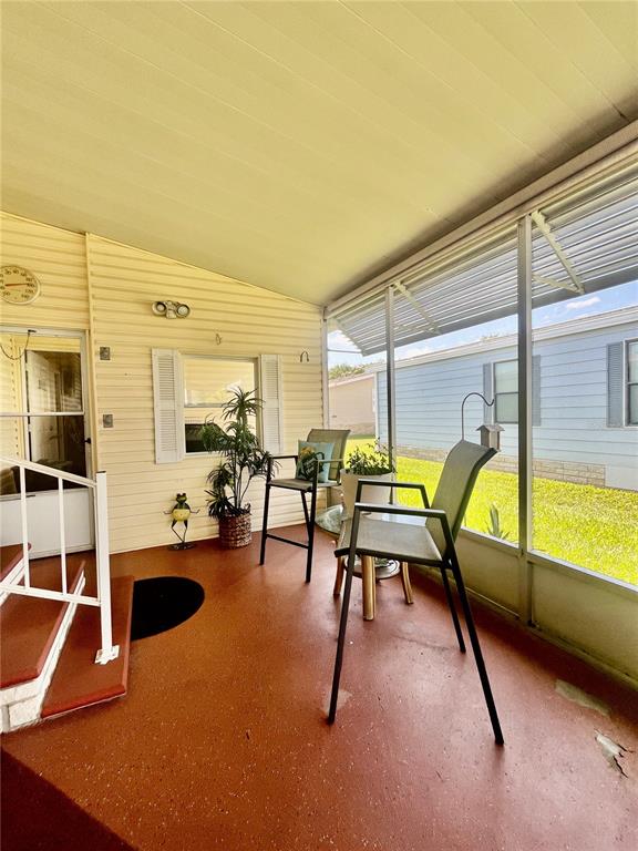 A screened-in porch features a red floor, two chairs, a potted plant, and siding — 5716 PAWNEE STREET, ZEPHYRHILLS, FL