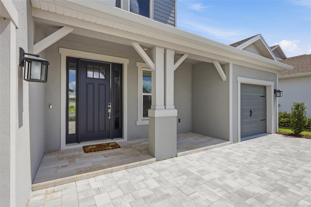 A gray house exterior features a covered porch, a dark front door, and a paver driveway — 8494 SNOWFALL STREET, SARASOTA, FL