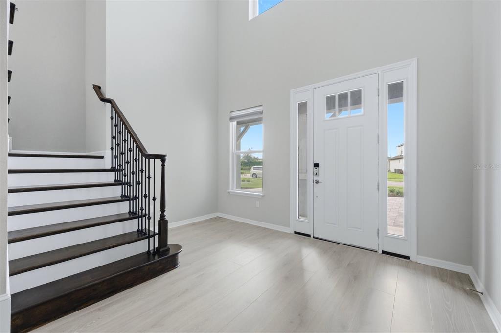 A bright entryway features light wood-look flooring, a staircase with dark railings, and a front door — 8494 SNOWFALL STREET, SARASOTA, FL