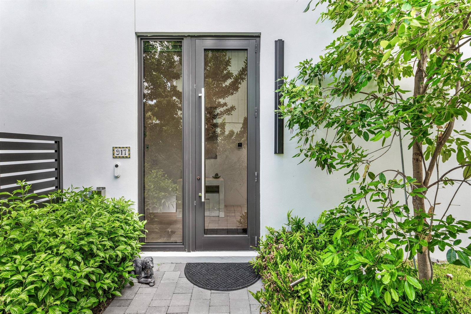 A modern glass-paneled front door with a vertical handle is set into a white exterior wall — 917 NE 8th Avenue, Delray Beach FL 33483, DELRAY BEACH, FL