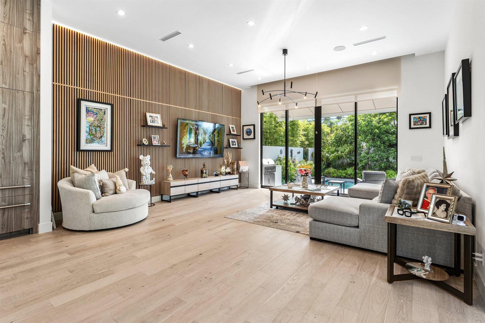 A modern living room features a slatted wood accent wall, light hardwood floors, and floor-to-ceiling windows — 917 NE 8th Avenue, Delray Beach FL 33483, DELRAY BEACH, FL