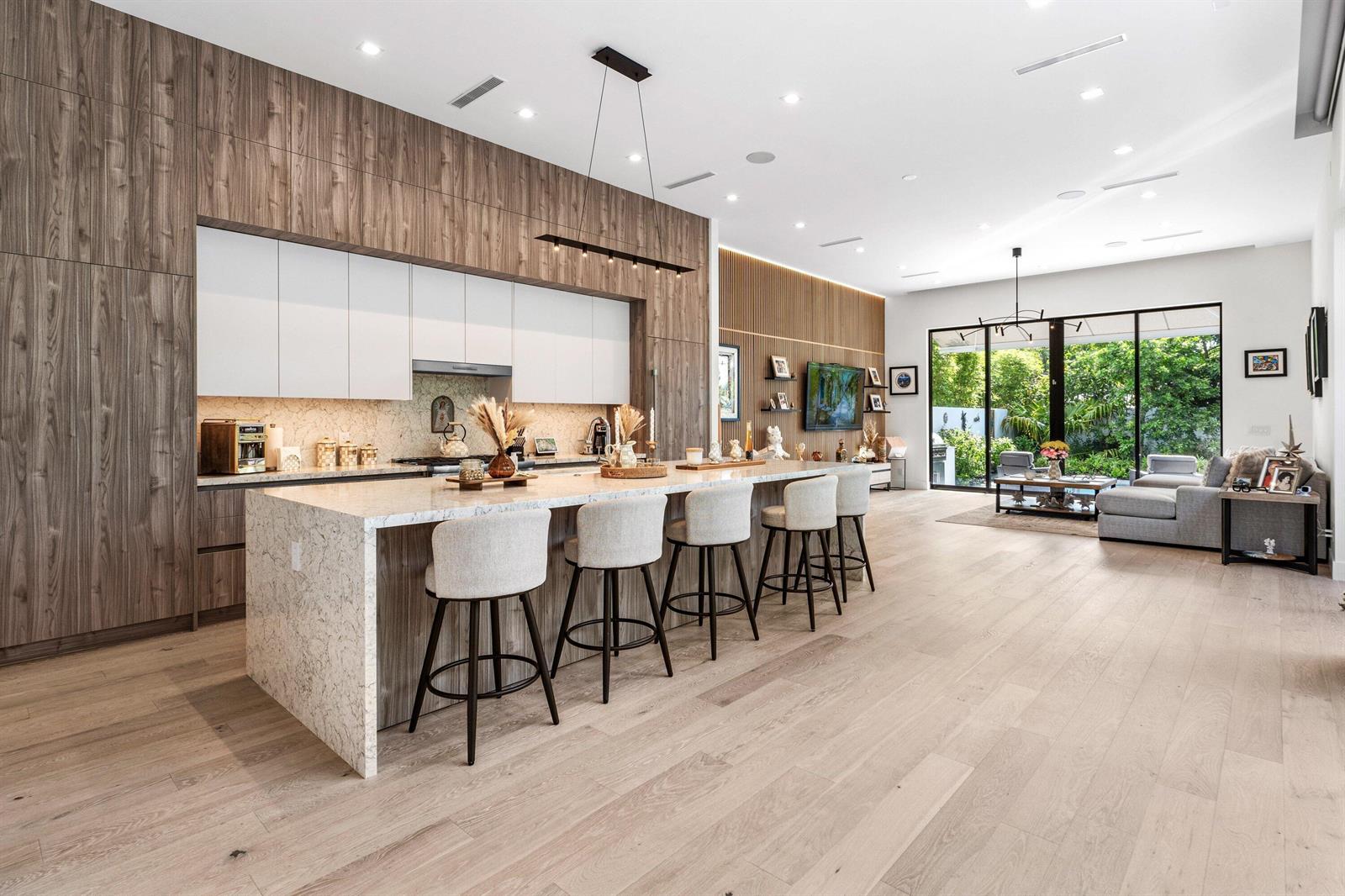 A modern open-concept kitchen features wood cabinetry, a large stone island, and light hardwood floors — 917 NE 8th Avenue, Delray Beach FL 33483, DELRAY BEACH, FL