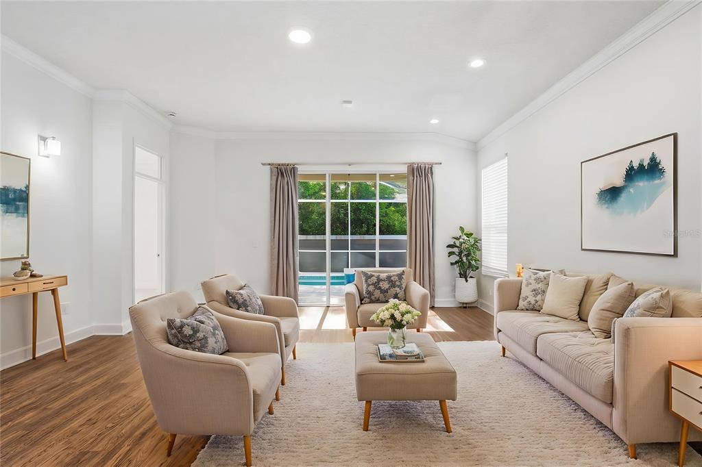 A bright living room features beige furniture, a white rug, and sliding glass doors to a pool — 19409 MELODY FAIR PLACE, LUTZ, FL