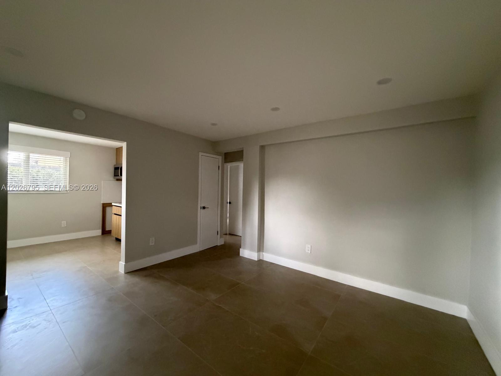 An empty room with light gray walls, large tile flooring, and a doorway to a kitchen — 1844 NW 19th St # 1, Miami FL 33125, MIAMI, FL