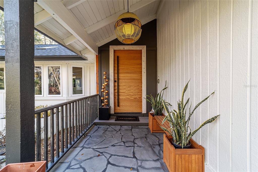 A covered porch features a wood front door, stone flooring, and a hanging woven light — 4400 SW 20TH AVENUE, OCALA, FL