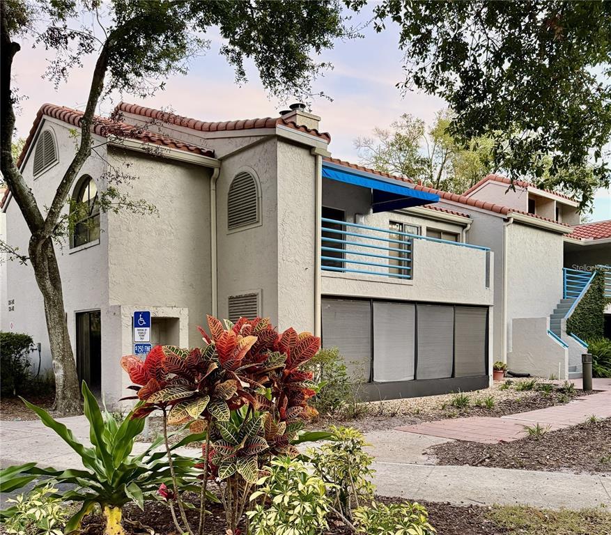 A two-story stucco building with a tiled roof, a blue-railed balcony, and a screened patio — 1000 WINDERLEY PLACE UNIT 239, MAITLAND, FL