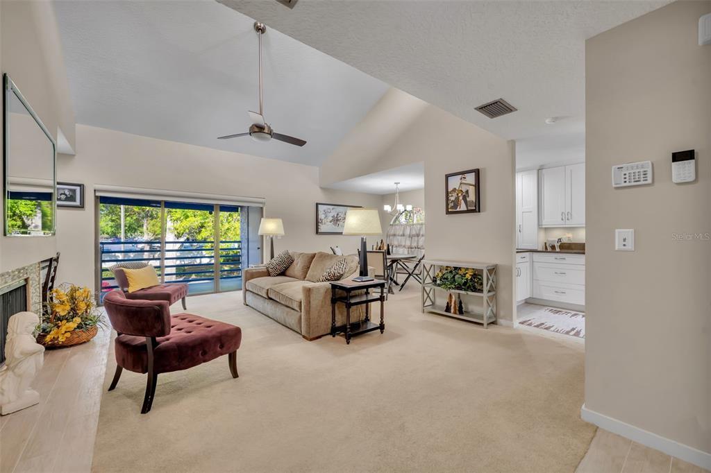 A living room with a vaulted ceiling, beige carpet, and an adjacent kitchen area — 1000 WINDERLEY PLACE UNIT 239, MAITLAND, FL