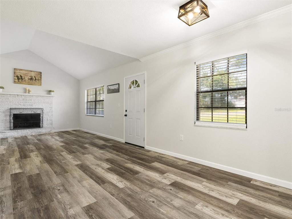 A living room features a white brick fireplace, wood-look flooring, and a vaulted ceiling — 4343 NW 80TH AVENUE UNIT 7, OCALA, FL