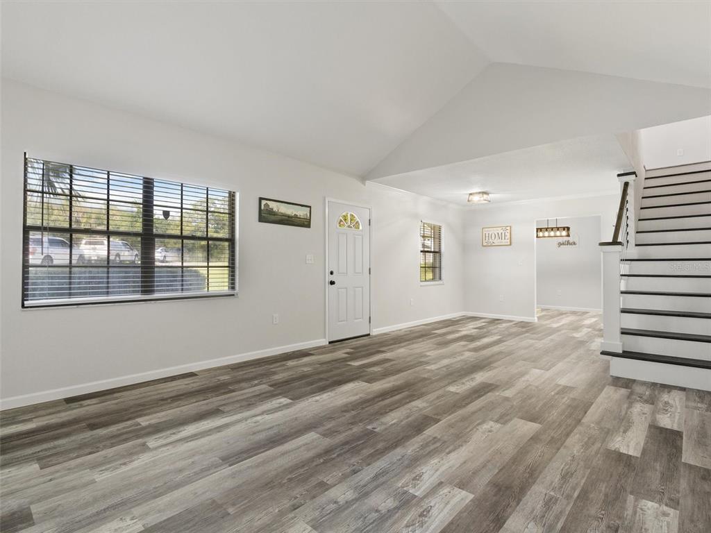 A living room with wood-look flooring, a vaulted ceiling, a front door, and a staircase — 4343 NW 80TH AVENUE UNIT 7, OCALA, FL