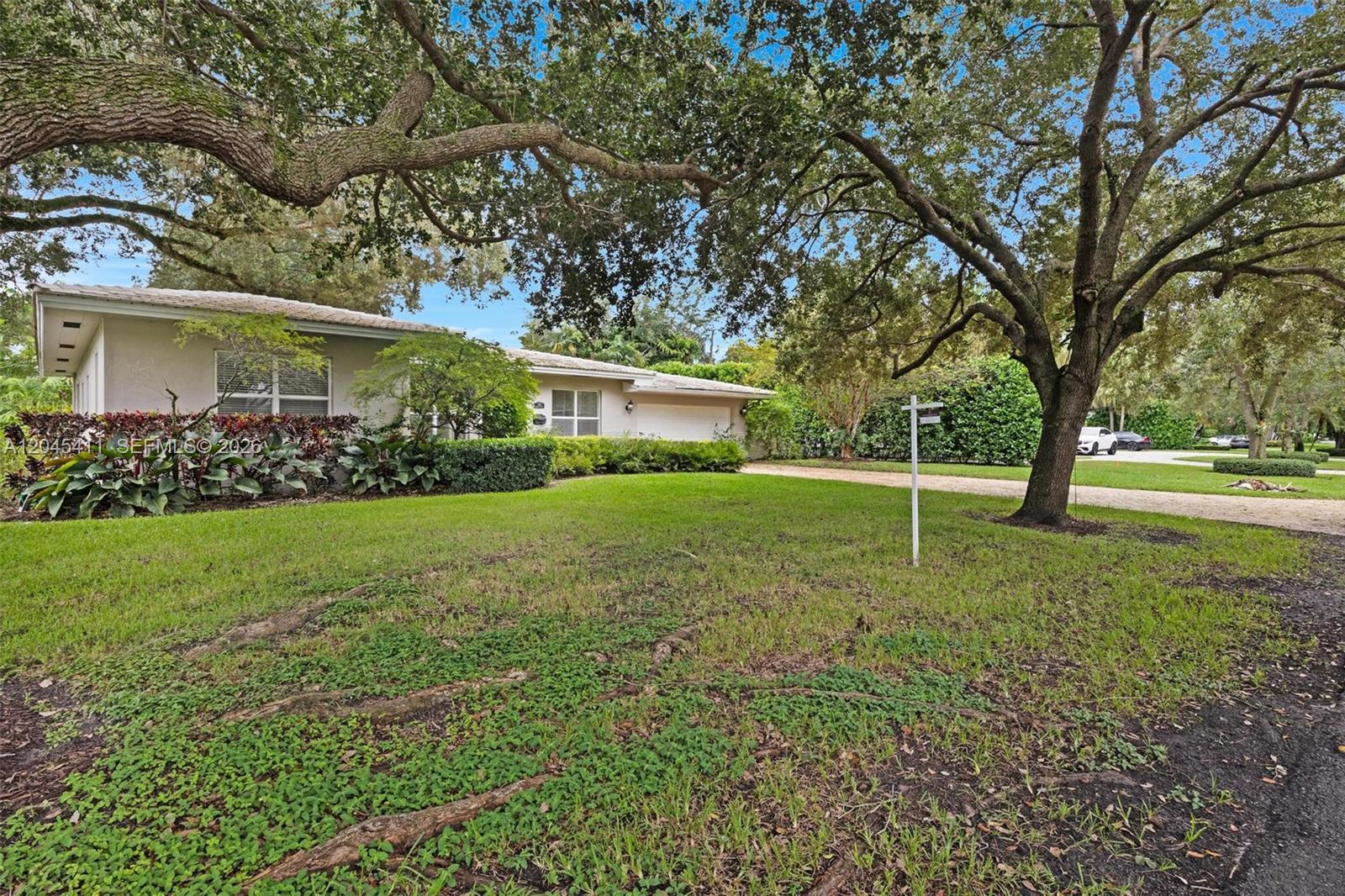 A single-story house with a light-colored exterior sits behind a large lawn and trees — 1246 Algardi Ave, Coral Gables FL 33146, CORAL GABLES, FL