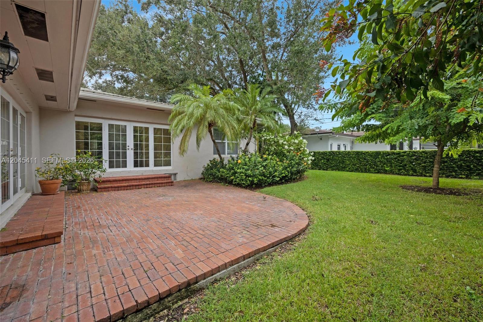 A brick patio sits outside a house with white French doors and a grassy yard — 1246 Algardi Ave, Coral Gables FL 33146, CORAL GABLES, FL