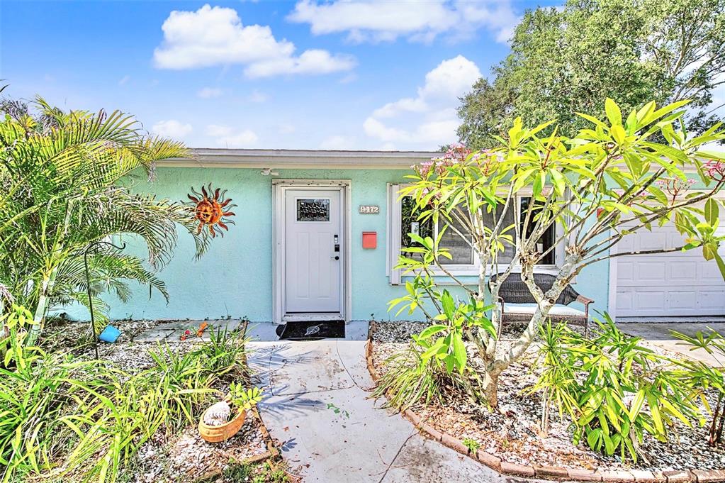 The exterior of a light blue house features a white front door and landscaping — 9472 TREASURE LANE NE, ST PETERSBURG, FL