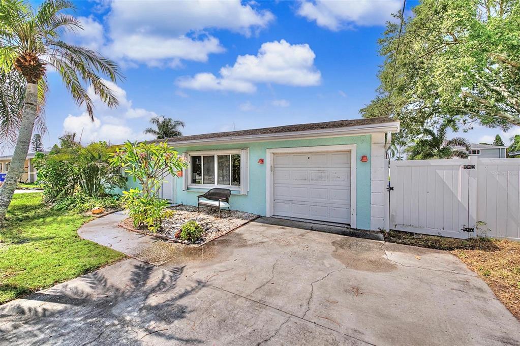 A light blue single-story house features a concrete driveway, a garage, and a white fence — 9472 TREASURE LANE NE, ST PETERSBURG, FL