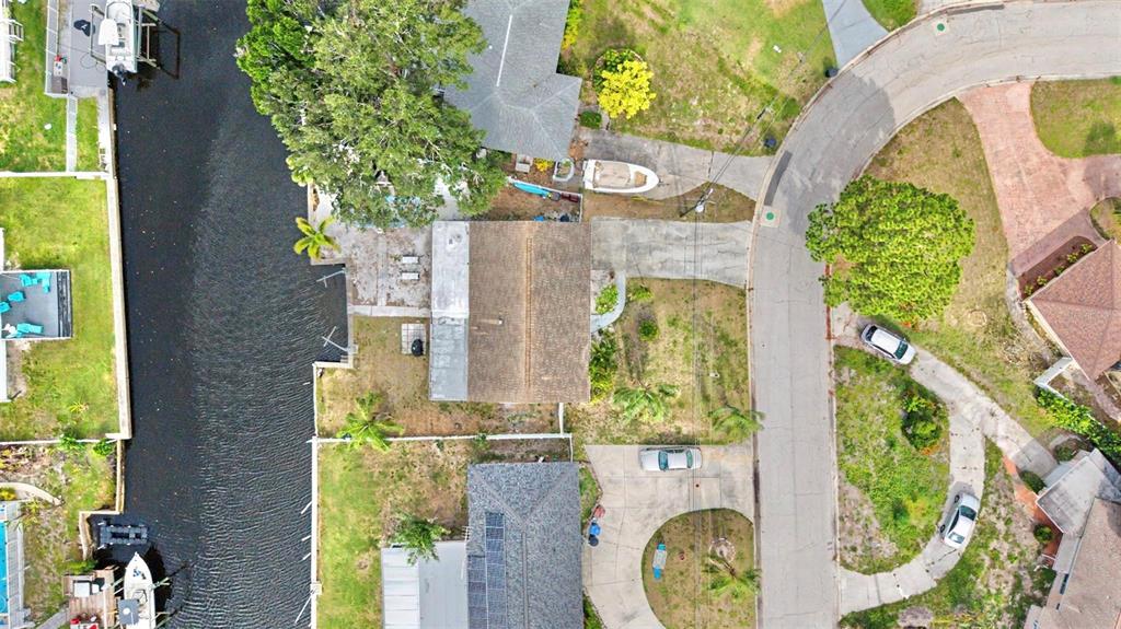An aerial view shows a house with a canal, driveway, and surrounding residential properties — 9472 TREASURE LANE NE, ST PETERSBURG, FL