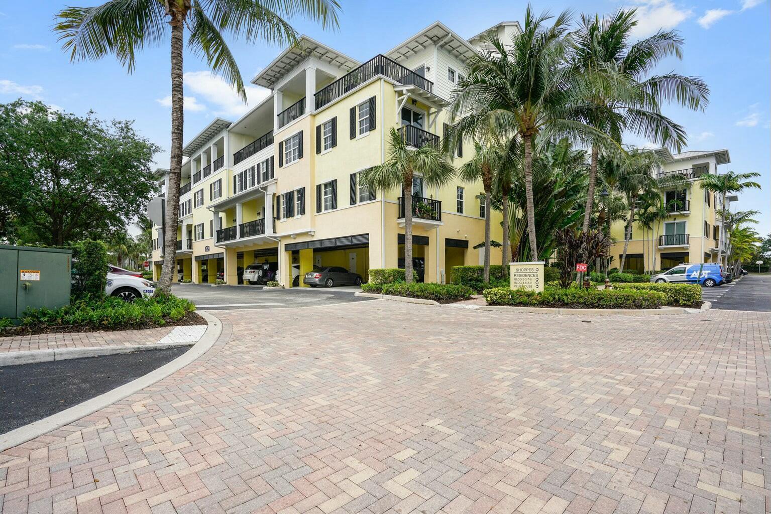 A multi-story yellow apartment building with covered parking and palm trees in a paved lot — 3120 E Latitude Circle # 206, Delray Beach FL 33483, DELRAY BEACH, FL