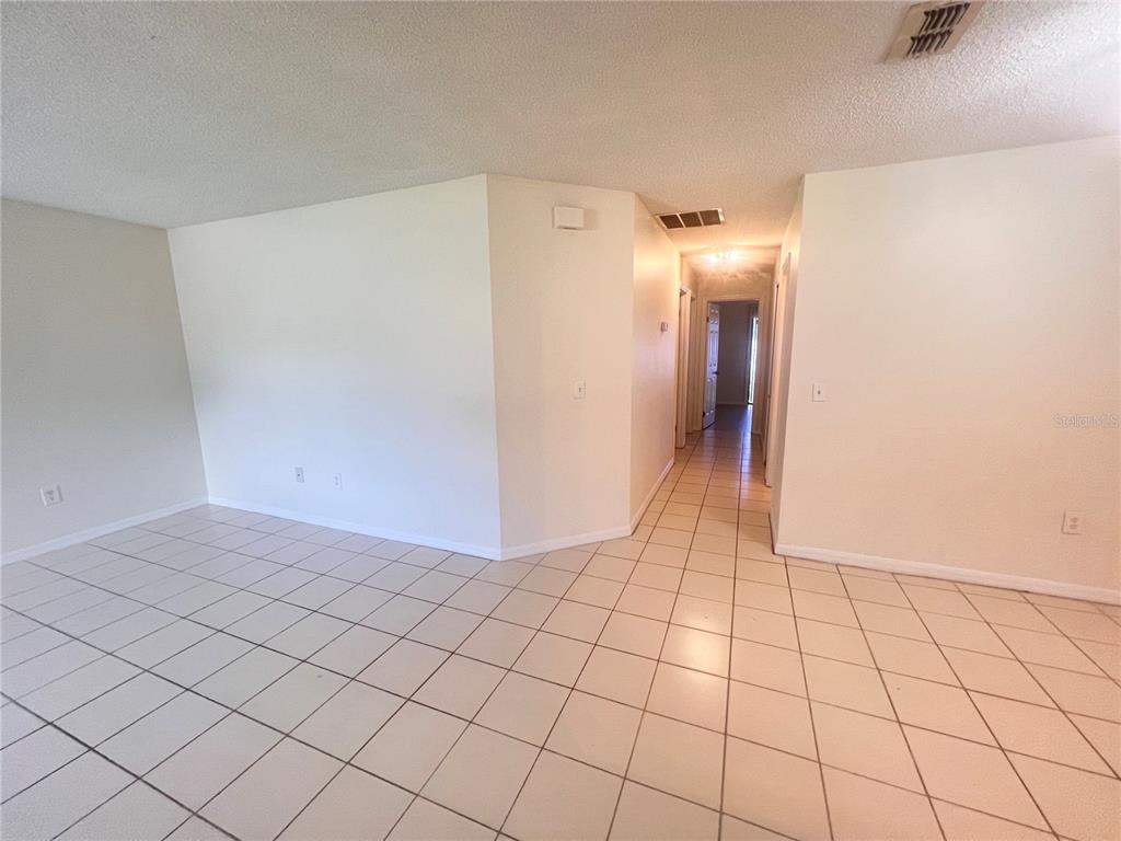 An empty room with white walls and light-colored square floor tiles leads to a hallway — 73 PROVIDENCE LANE UNIT A, PALM COAST, FL