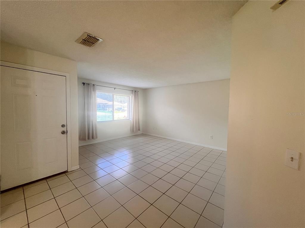 An empty room with white walls, beige tile flooring, and a single window with curtains — 73 PROVIDENCE LANE UNIT A, PALM COAST, FL