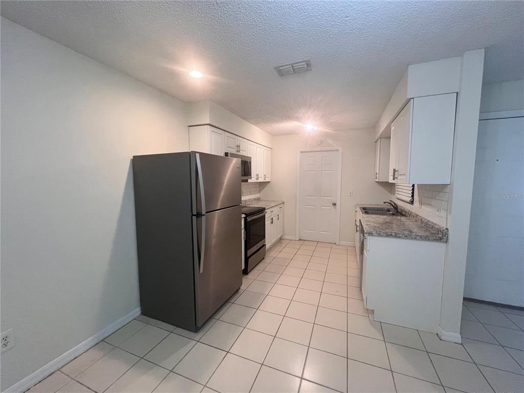A kitchen features white cabinets, granite-look countertops, stainless steel appliances, and light-colored tile flooring — 73 PROVIDENCE LANE UNIT A, PALM COAST, FL