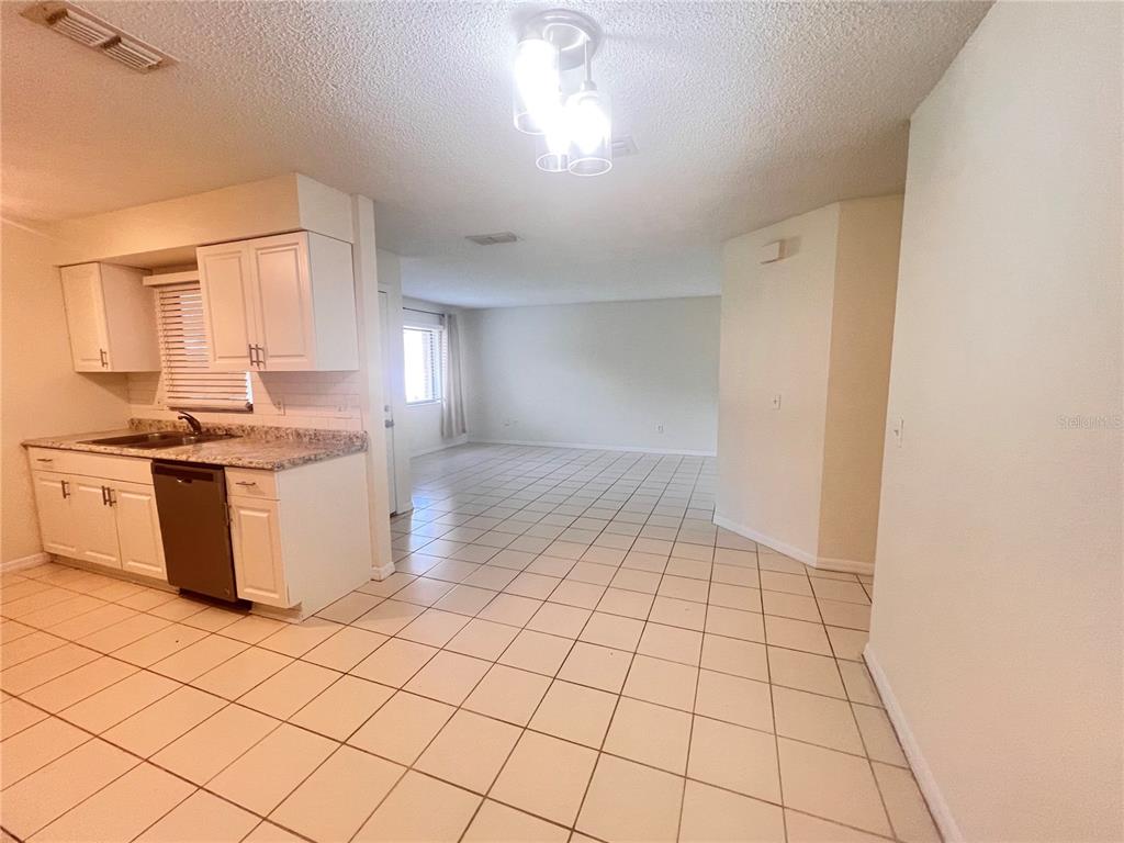 A kitchen with white cabinets and tile flooring opens into a spacious living area — 73 PROVIDENCE LANE UNIT A, PALM COAST, FL