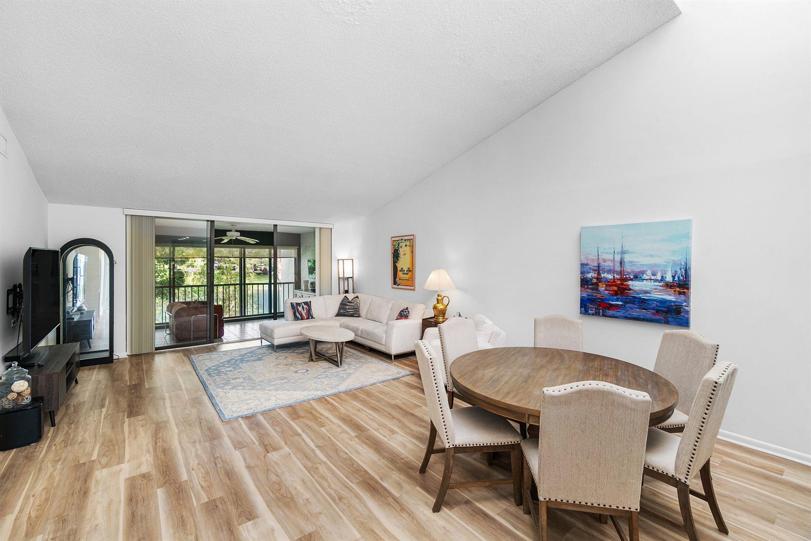 A living and dining area features wood-look flooring, a white sectional sofa, and a balcony — 61 Eastgate Drive # D, Boynton Beach FL 33436, BOYNTON BEACH, FL