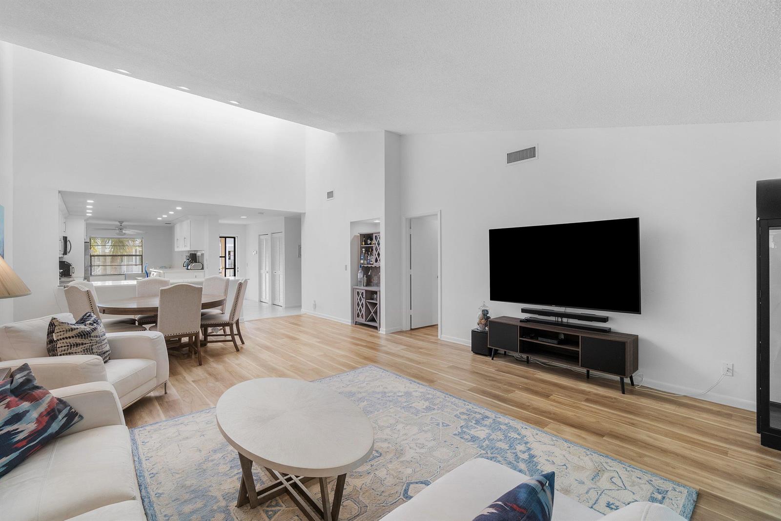 A bright living room features high ceilings, light wood flooring, and an open dining area — 61 Eastgate Drive # D, Boynton Beach FL 33436, BOYNTON BEACH, FL