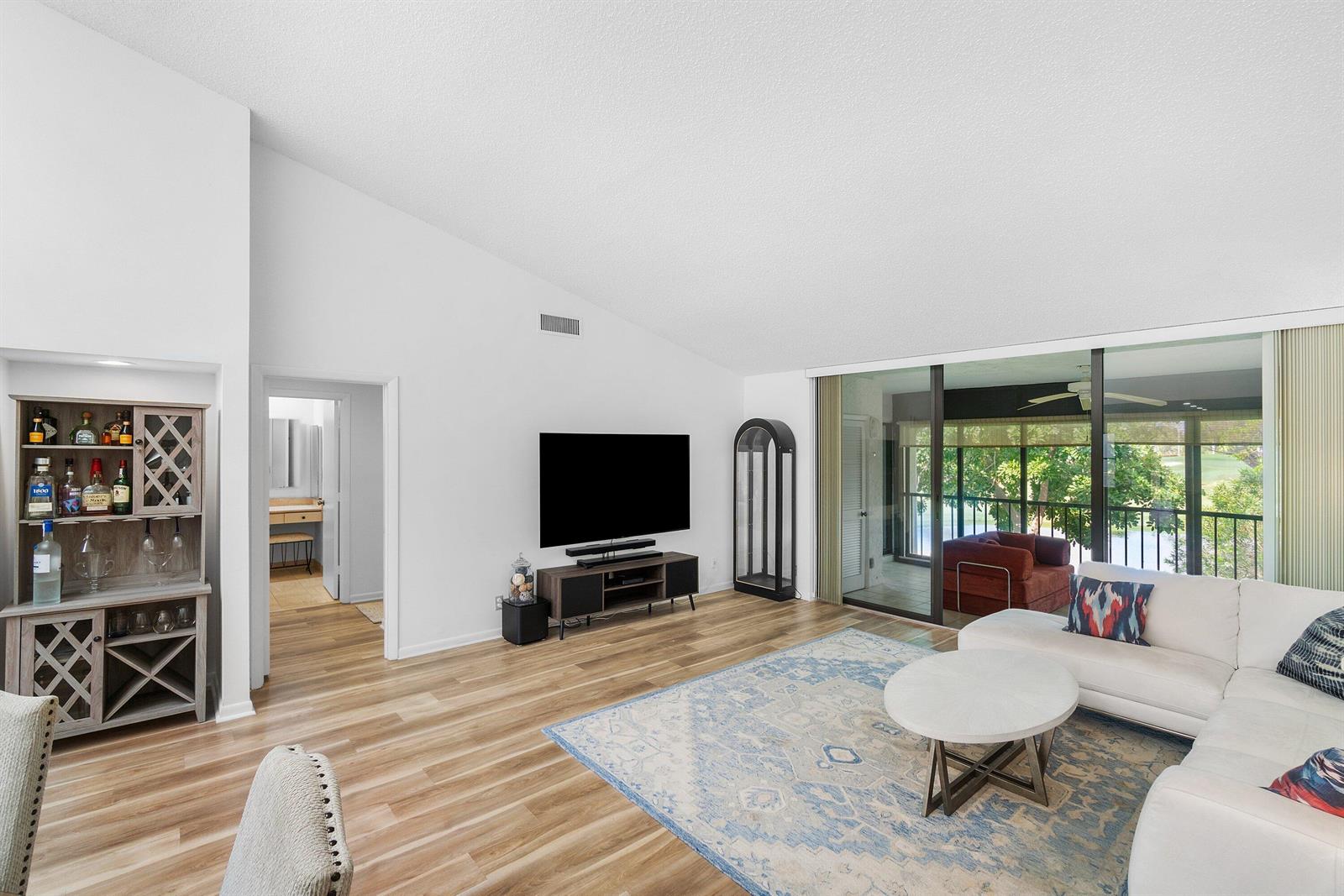A living room with light wood floors, a white sectional, and a view of trees — 61 Eastgate Drive # D, Boynton Beach FL 33436, BOYNTON BEACH, FL