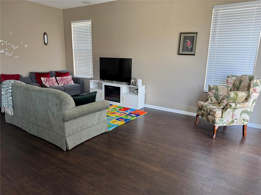 A living room features dark wood-look flooring, a gray sofa, a floral armchair, and a television — 435 STONE BRIAR DRIVE, RUSKIN, FL